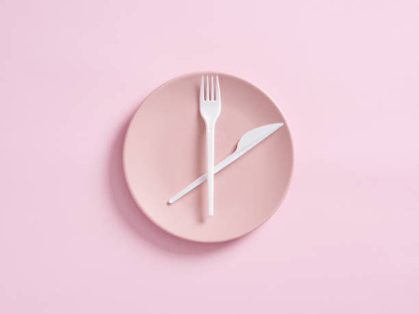istock Knife and fork on pink plate designed as clock. Intermittent fasting, lunchtime, weight loss, meal plan or diet 1407974354