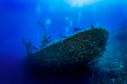 A group of unrecognizable scuba divers explores a sunken shipwreck at the bottom of the Aegean Sea in Greece, Kea island