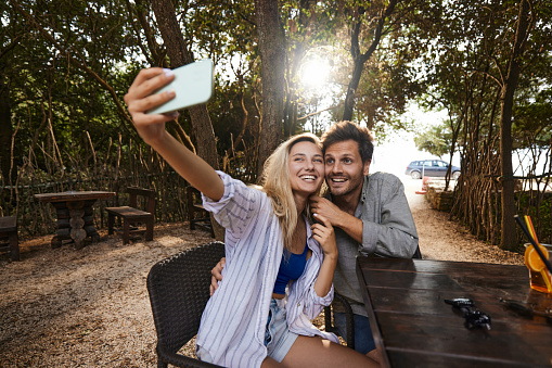 Happy couple enjoying while taking a selfie with cell phone during spring day in a café.