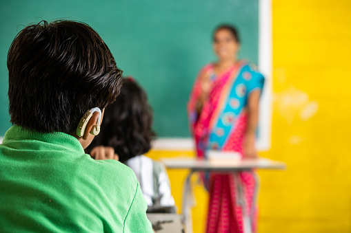kid with hearing aid machine listening lesson at classroom showing with copy space - concept of aspiration, education and learning