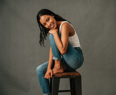 Relaxed African American sitting on a high chair resting her head on her knee dressed casually in her jeans. High quality photo