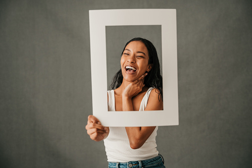 Laughing smiling close up of multiethnic female holding a frame with long dark hair in casual wear . High quality photo