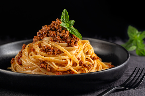 Spaghetti or linguine with meat and tomato sauce bolognese on a black plate and dark background. Close-up.