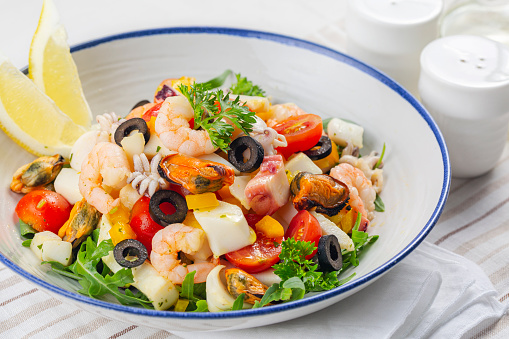 Close up of Italian mixed seafood salad. Insalata di mare. Calamari, shrimp, clams, tomatoes, bell pepper, parsley and olives.