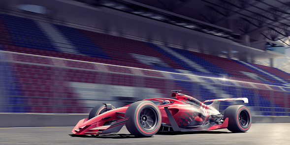 A contemporary generic red, black and silver race car driven at high speed on a racetrack past an empty grandstand. The car is moving at high speed with motion blur to the wheel and background.