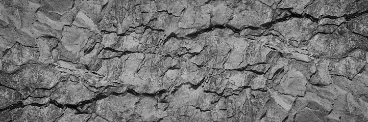 Dark gray rock texture. Rough mountain surface with cracks. Close-up. Stone background with space for design. Black White. Grunge. Web banner. Wide. Panoramic.