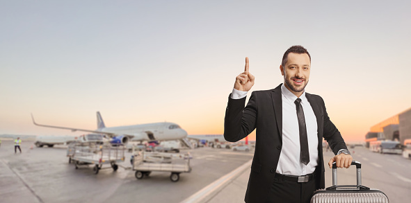 Businessman with a suitcase standing on an airport apron and pointing up