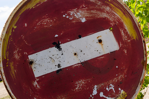 Weathered, scratched and dirty old red and white round No entry road sign with muddy road leading.