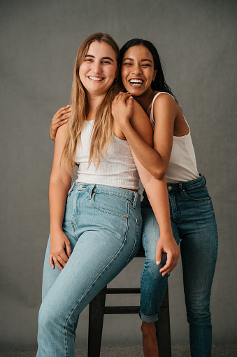 Two female friends in there casual wear posing in the studio sharing a stool. High quality photo