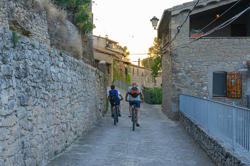 Talamanca, Bages - July 9, 2022: Two mountain bikers riding down a stone-floored village street