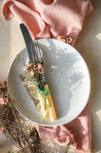 istock Easter table setting background with plate, cutlery set and pink flowers. Empty plate, advertising, menu. Bright sunlight and hard shadows photography. 1407985935