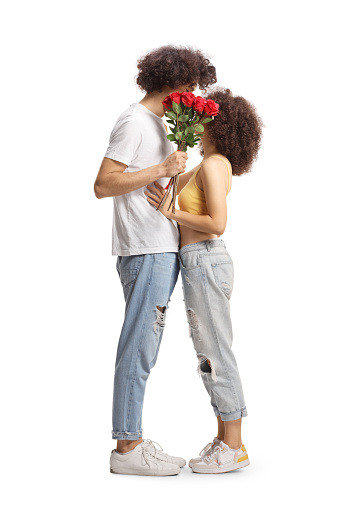 Full length profile shot of casual young couple hugging and holding a bunch of red roses isolated on white background