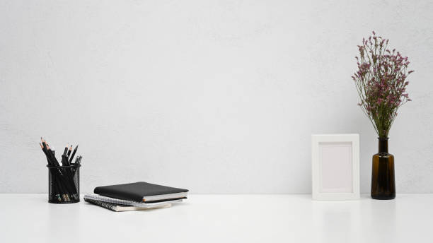 istock Minimal workplace with picture frame, pencil holder and books on white table. 1407987164