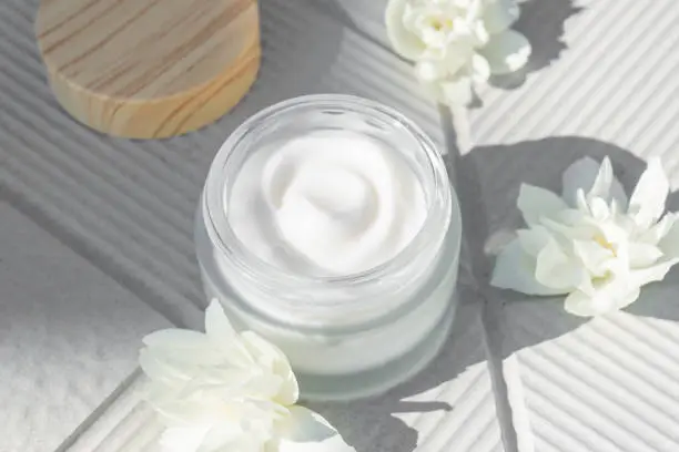 Spa concept. Cream in a glass jar with jasmine flowers on whiteconcrete background. copy space. Close-up