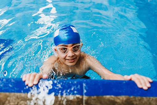 latin child boy swimmer wearing cap and goggles in a swimming training at the Pool in Mexico Latin America