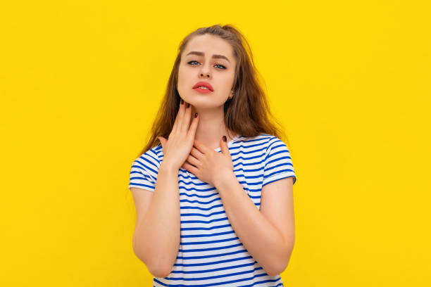 halsschmerzen. junge kranke frau mit halsschmerzen, leidet an schmerzhaftem schlucken, starken schmerzen im hals, berühren des halses mit der hand. indoor-studio auf gelbem hintergrund aufgenommen. gesundheitliche probleme - throat exam stock-fotos und bilder