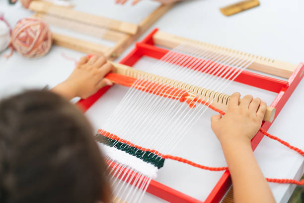 istock Girl weaving small rug with pattern at masterclass on weaving 1407990243