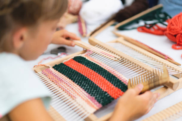 Girl weaving small rug with pattern at masterclass on weaving Girl weaving small rug with pattern at masterclass on weaving. Girl is studying how to weave on manual table loom. Process of creation. Handmade concept basket weaving stock pictures, royalty-free photos & images