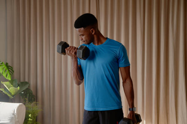 라운지에서 집에서 운동하는 흑인 아프리카 계 미국인 젊은 남성의 정면 모습은 체중과 덤벨, 이두박근 컬을 들어 올리고 몸매와 건강을 유지합니다. - ewan 뉴스 사진 이미지