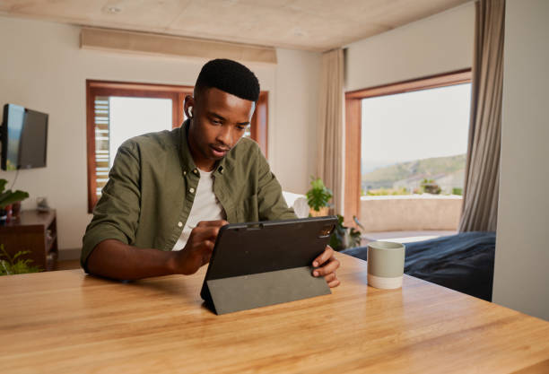 젊은 성인 아프리카 계 미국인 남성은 펜을 사용하여 전자 태블릿에 글을 씁니다. 집중적으로 앉아서 현대 가정에서 원격으로 일합니다. - ewan 뉴스 사진 이미지