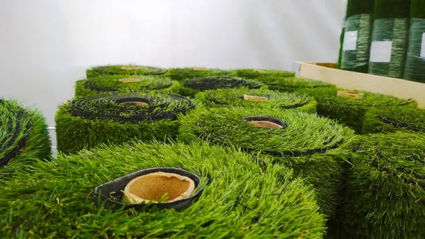 Photo of Rolls of green artificial grass carpet or wall in supermarket. Hypermarket for gardeners. Landscape design. Gardening. Goods for garden. Greenhouse. Environment conservation concept. Lawn turf.