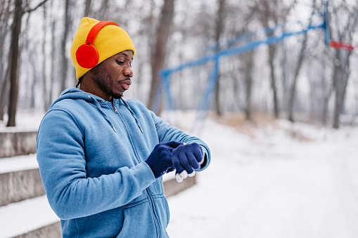 Handsome young black man checking his fitness activity on smart watch after training outdoors in winter on the snow.