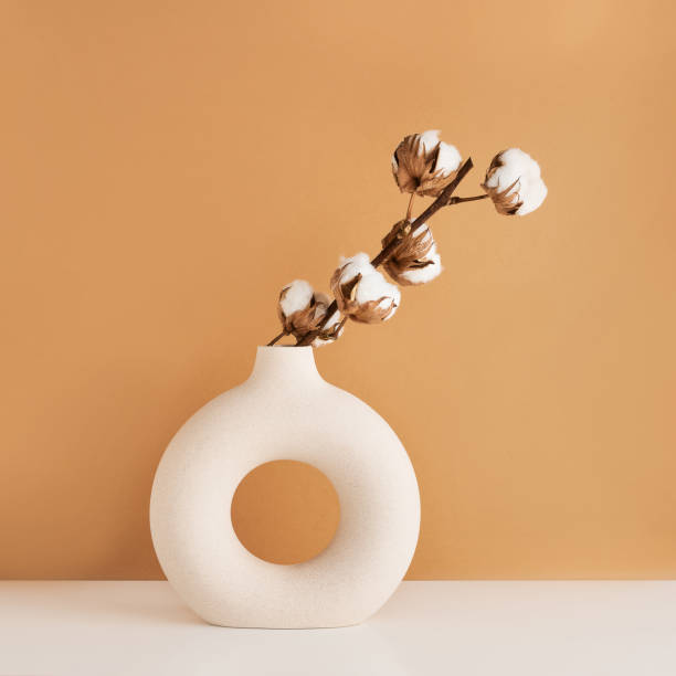 istock Round ceramic vase with a cotton branch on a white table by the brown wall. Copy space 1407997530