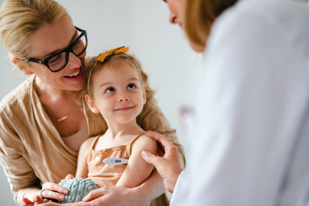 Portrait of an Adorable Girl Is Getting Her Temperature Checked at the Doctorâs Office Cute cheerful girl is sitting in her mom's lap in doctor's office. She is holding a toy while waiting for her temperature to be measured with a digital thermometer. Her mom is hugging her and smiling while an anonymous doctor is leaning towards them. girl patient stock pictures, royalty-free photos & images