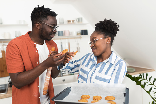 Young African American couple tasting just baked homemade cookies at their kitchen