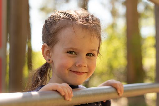 Little beautiful girl with braided pigtails has fun on the uneven bars in the park