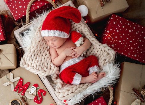 Charming newborn sleeping with toy in cradle between christmas presents