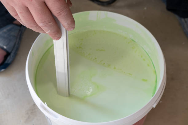 istock Worker's hands stir green paint before applying it, close-up. Bucket for mixing paints 1408006104