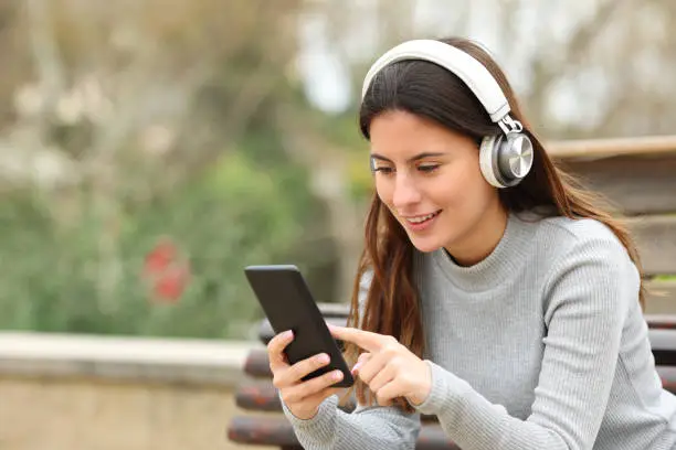 Happy teen using phone listening to music in a park