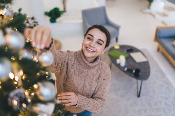istock Smiling woman decorating Christmas tree alone at home 1408009166