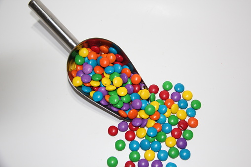 Colorful chocolate candies in a stainless steel measuring spoon on a white background , top view.