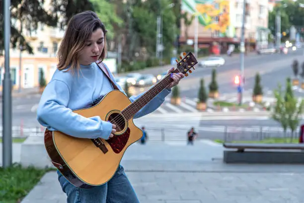 A young woman musician plays the acoustic guitar and sings on the street.