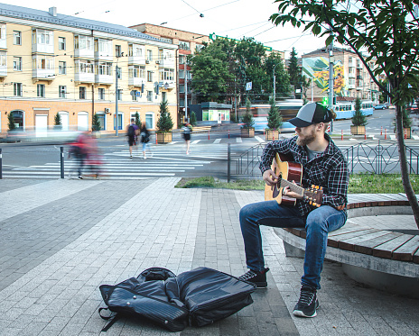 A man street musician with a beard and a cap plays the acoustic guitar.