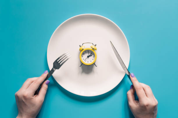 istock Hands holding knife and fork above alarm clock on a plate on blue background. 1408013657