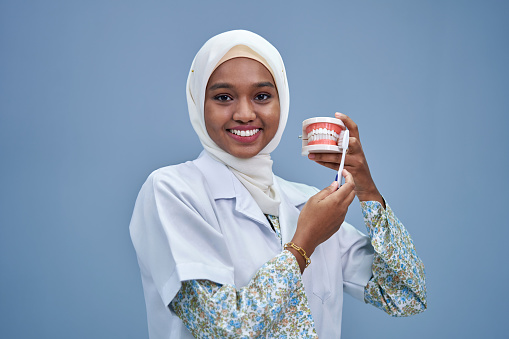 dentist hijab holding model tooth against gray background