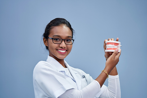 female dentist with eyewear holding  model tooth against gray wall