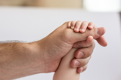 Baby's little hand holding the hand of his father