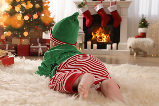 Baby wearing cute elf costume in room decorated for Christmas