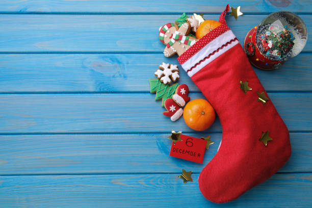 istock December, 6 - Saint Nicholas Day. Stocking with sweets, paper tag, festive decor and space for text on blue wooden table, flat lay 1408022819