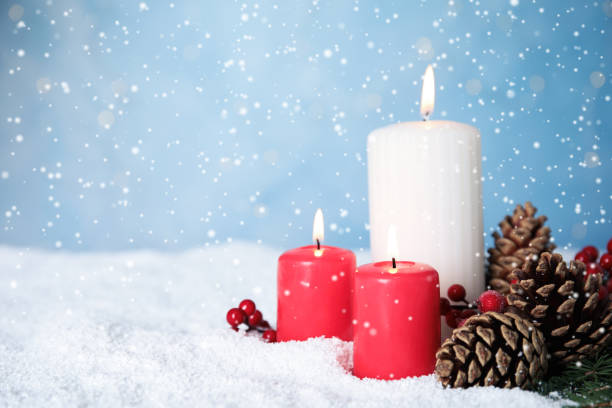 istock Snow falling on burning candles and pine cones against light blue background, space for text. Christmas eve 1408022910