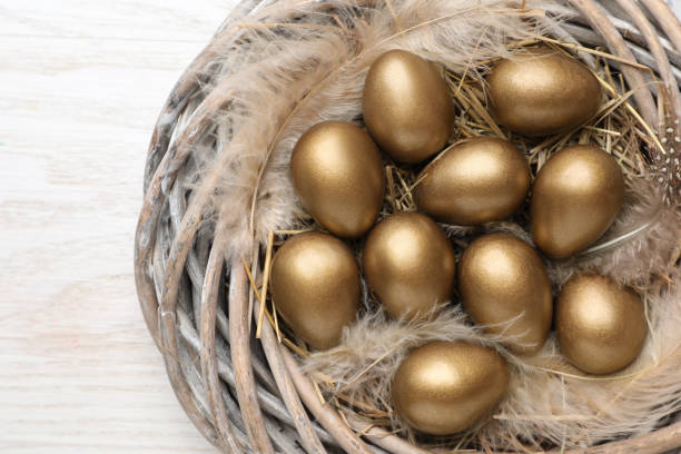 istock Many golden eggs in nest on white wooden table, top view 1408024229