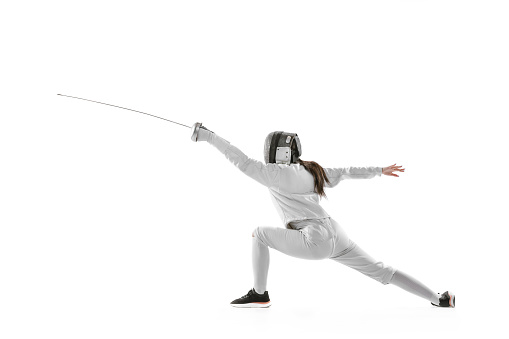 Dynamic portrait of female fencer in sports costume and fencing mask holding rapier in hand and training isolated on white background. Sport, youth, healthy lifestyle, achievements. Copy space for ad