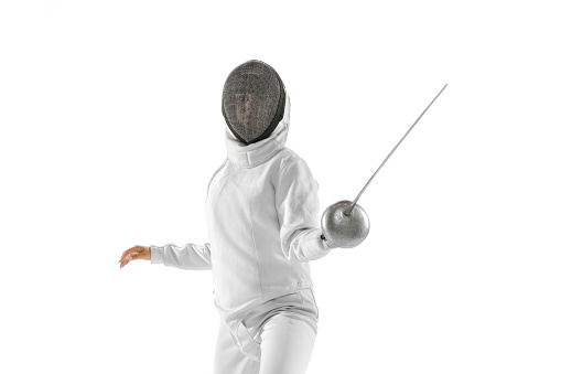 Front view. One sportsman, female fencer in white fencing costume in action, motion isolated on white background. Sport, youth, hobbies, achievements, goal. Girl practicing with rapier