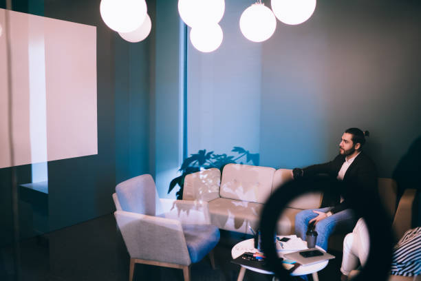 Through decorated glass view of office workers in formal wear lying on couch and armchair while watching presentation at meeting room
