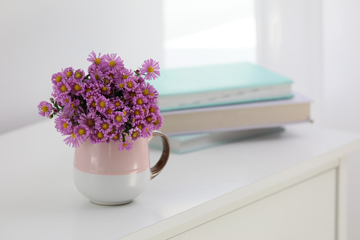 Cup with beautiful flowers on white table in light room. Space for text