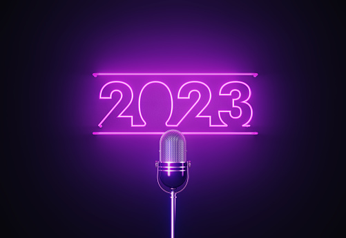Purple neon light writes 2023 above a silver colored microphone over black background. Horizontal composition with copy space.
